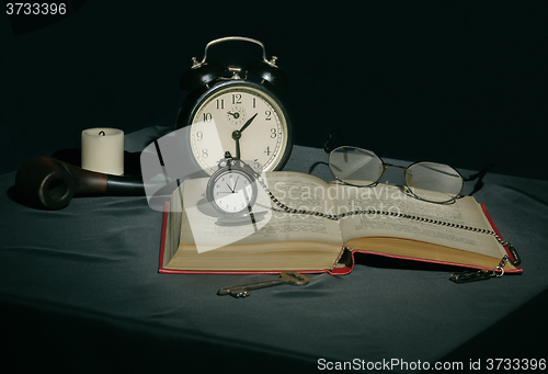 Image of Still life with a book and clocks in dark colors