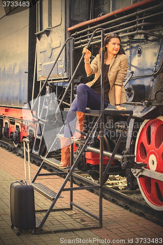 Image of pretty middle-aged woman with luggage near the old steam locomot