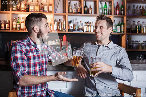 Image of Happy friends drinking beer at counter in pub