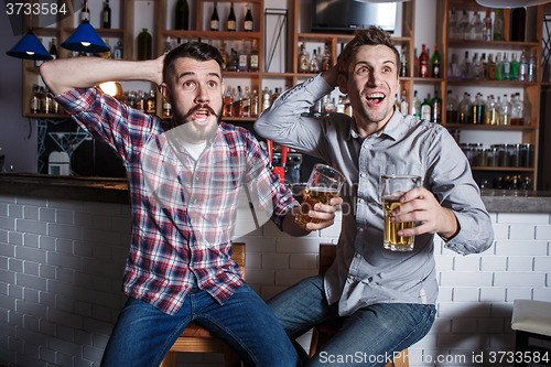 Image of Young people with beer watching football in a bar