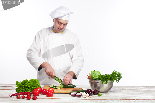 Image of Chef cutting a green cucumber in his kitchen
