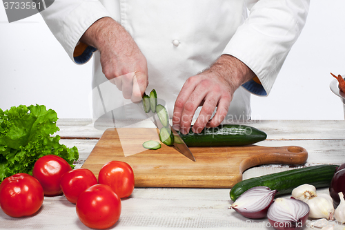 Image of Chef cutting a green cucumber in his kitchen