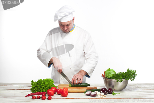 Image of Chef cutting a green cucumber in his kitchen
