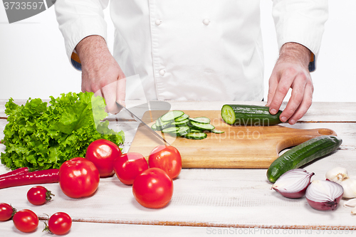 Image of Chef cutting a green cucumber in his kitchen