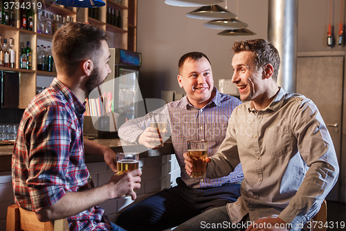 Image of Happy friends drinking beer at counter in pub