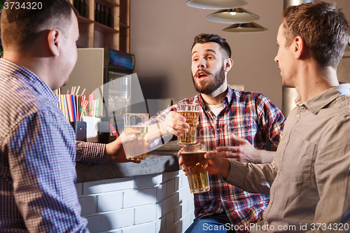 Image of Happy friends drinking beer at counter in pub