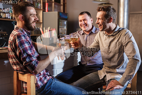 Image of Happy friends drinking beer at counter in pub