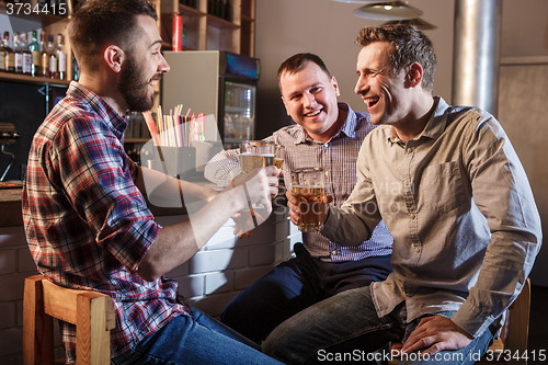 Image of Happy friends drinking beer at counter in pub