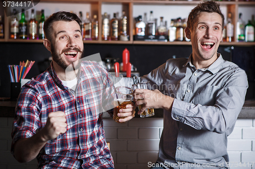 Image of Young people with beer watching football in a bar
