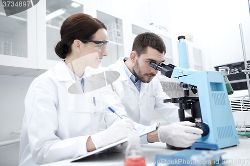 Image of scientists with clipboard and microscope in lab