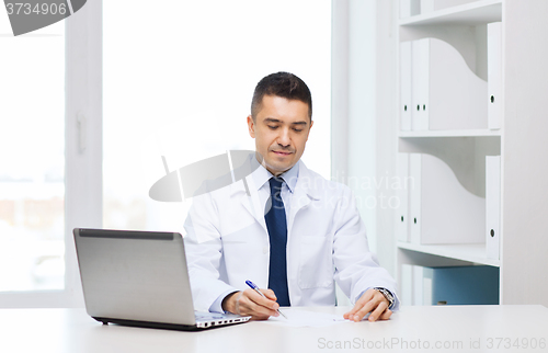 Image of smiling male doctor with laptop in medical office