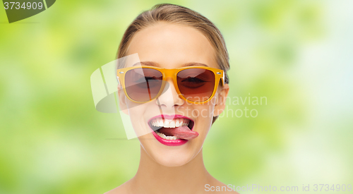 Image of happy young woman in sunglasses showing tongue