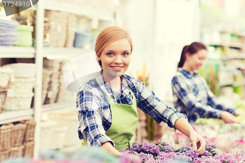 Image of happy woman taking care of flowers in greenhouse