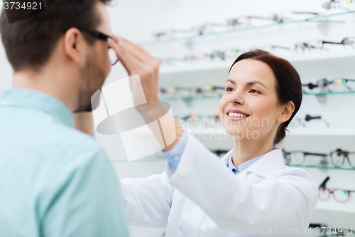 Image of optician putting on glasses to man at optics store