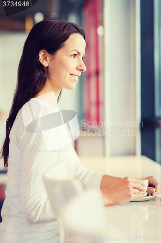 Image of smiling young woman drinking coffee at cafe
