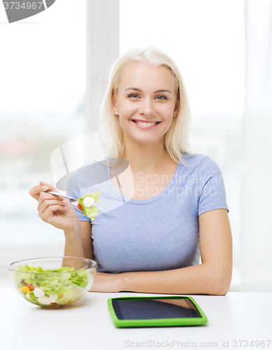 Image of smiling woman eating salad with tablet pc at home