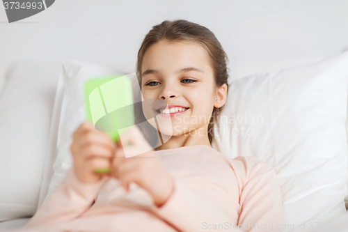 Image of happy girl lying in bed with smartphone at home