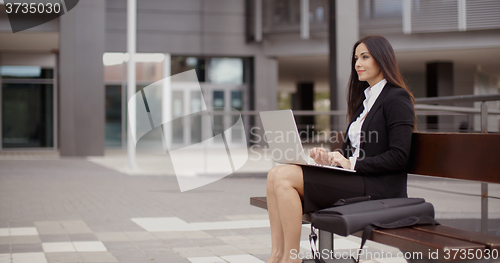 Image of Woman sitting with laptop on bench outdoors