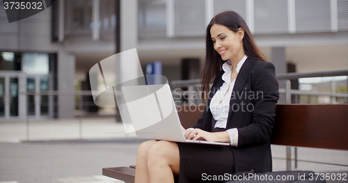 Image of Woman sitting with laptop on bench outdoors