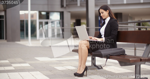 Image of Woman sitting with laptop on bench outdoors