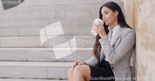 Image of Grinning woman on stairs drinking coffee