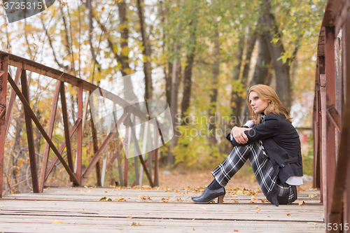 Image of Sad girl sitting on a bridge in the forest