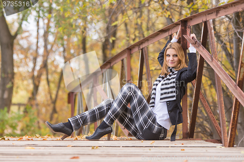 Image of Happy girl sitting on a bridge in the forest and looking at the frame