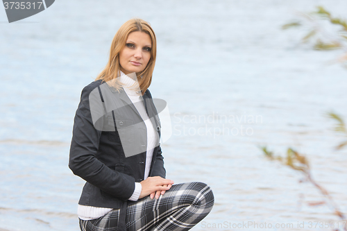 Image of Young beautiful girl sat down by the river in the warm autumn weather