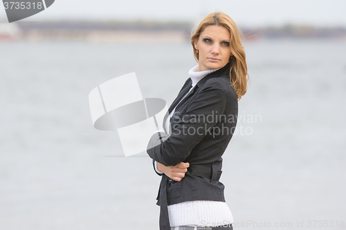 Image of Beautiful sad girl standing by the river in the warm autumn weather