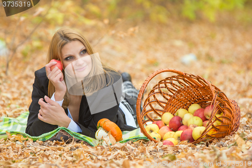 Image of Young beautiful girl lies on the on the foliage in the autumn forest and dreaming holding an apple and looking to the right