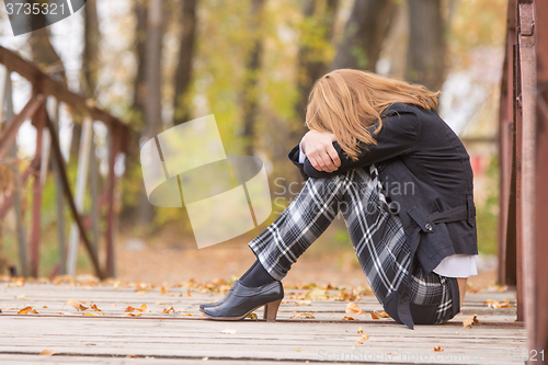 Image of Sad girl sitting on a bridge with her head resting on his knees