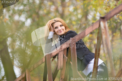 Image of Young beautiful girl standing on the bridge, leaning on the railing and looking pensively into the distance