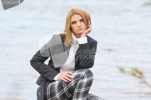 Image of Beautiful sad girl sat by the river in the warm autumn weather