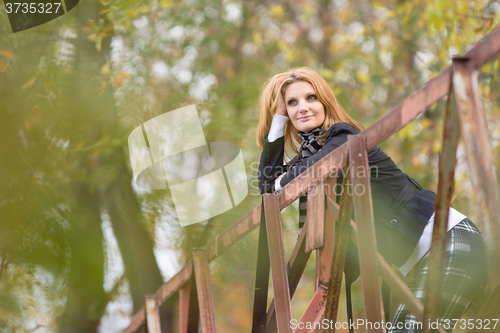 Image of Young beautiful girl standing on the bridge and happily leaning on the railing