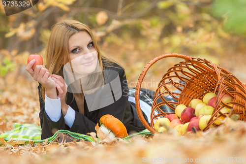 Image of Young beautiful girl lies on the on the foliage in the autumn forest and holding an apple in her hand