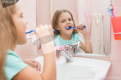 Image of Six year old girl cleans the upper lateral teeth look in the mirror in the bathroom
