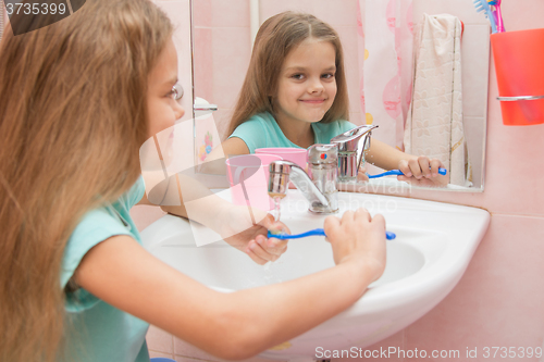 Image of The girl washes a toothbrush under the tap