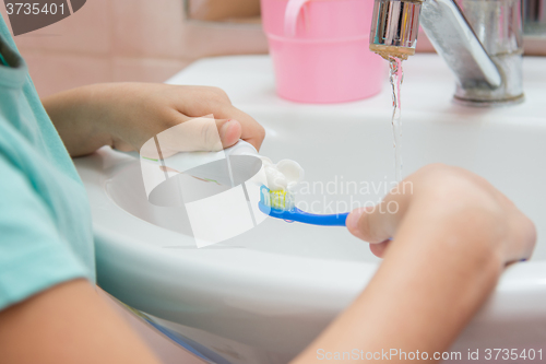 Image of The child squeezes the toothpaste from a tube on toothbrush