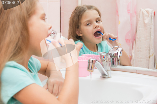 Image of Six year old girl cleans the lower lateral teeth look in the mirror in the bathroom