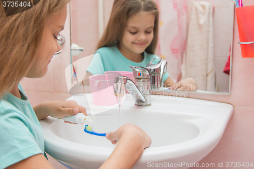 Image of Girl before cleaning teeth squeezing toothpaste out of a tube on toothbrush