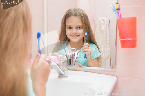 Image of Six year old girl opening her mouth treats teeth in reflection in a mirror, while in the bathroom