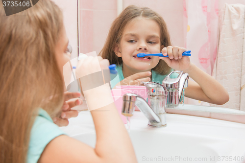 Image of Six year old girl having fun brushing his teeth look in the mirror in the bathroom