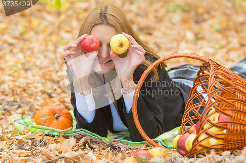 Image of Young beautiful girl lying on the leaves in the autumn forest in the fun and put the apples to the eyes