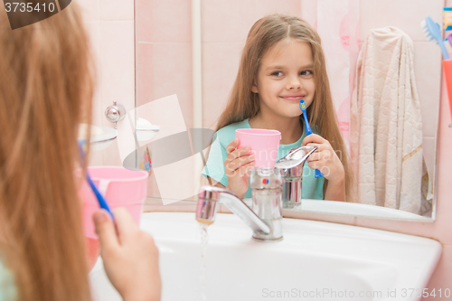 Image of Girl standing with a toothbrush and a glass in the bathroom