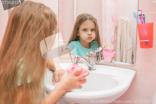 Image of Girl rinse your mouth in the bathroom and look in the frame