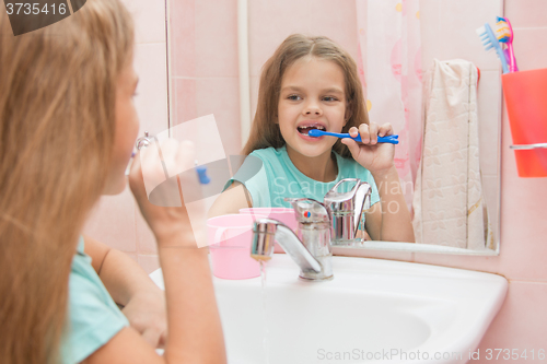 Image of Six year old girl cleans the lower front teeth look in the mirror in the bathroom