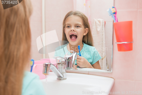 Image of Six year old girl opening her mouth treats teeth in reflection in a mirror, while in the bathroom