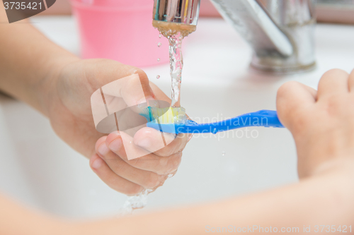 Image of Child washes toothbrush under running water, close-up