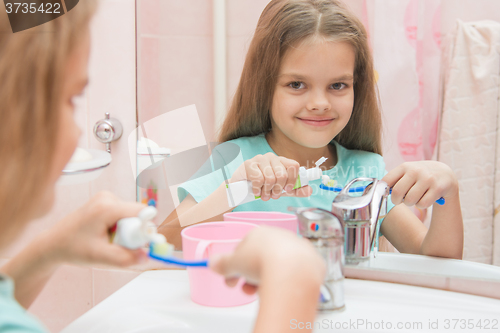 Image of Six year old girl squeezes the toothpaste from a tube on toothbrush