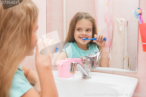 Image of Six year old girl brushing the front teeth look in the mirror in the bathroom